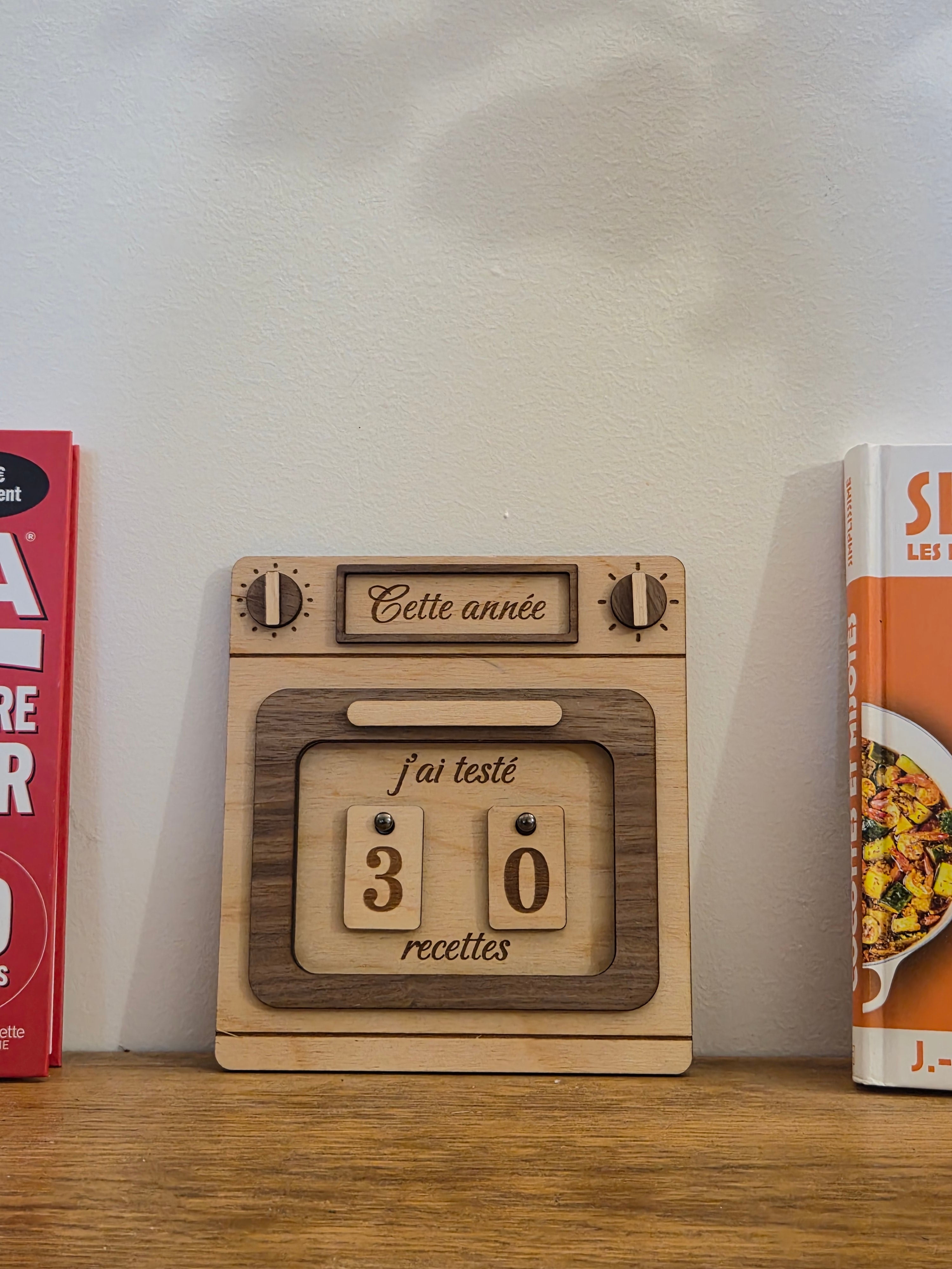 Tableau en contreplaqué pour suivre les commandes annuelles avec plaques modulables, posé sur une étagère.